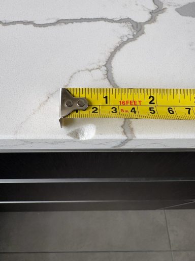 Cracked and chipped quartz worktop, which needs repairing. Quartz White kitchen worktop showing a large Chip on the edge, the tape measure is showing the size of the damaged edge.