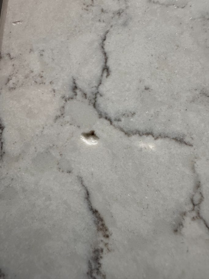 Before repair: impact damage to white quartz Quartz worktop repaired in leeds. Worktop surface was chipped the picture shows close up of damaged quartz kitchen worktop.
