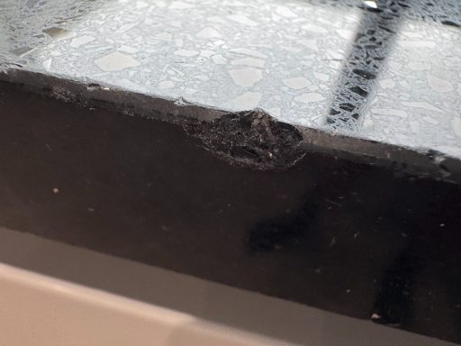 Chipped black quartz worktop at the edge Black Silestone kitchen worktop with a large section of the edge missing because a cup was dropped on it.