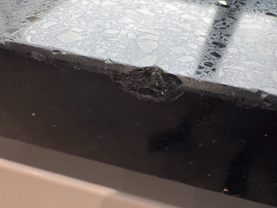 Before repair: chipped black Silestone edge Black Silestone kitchen worktop with a large section of the edge missing because a cup was dropped on it.