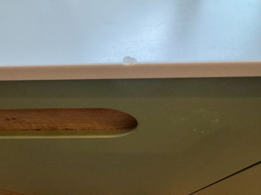 The edge of a Corian worktop is missing due to damage. The piece is missing. A speckled beige Corian worktop with a large chunk missing from the surface due to a large object being dropped on it.