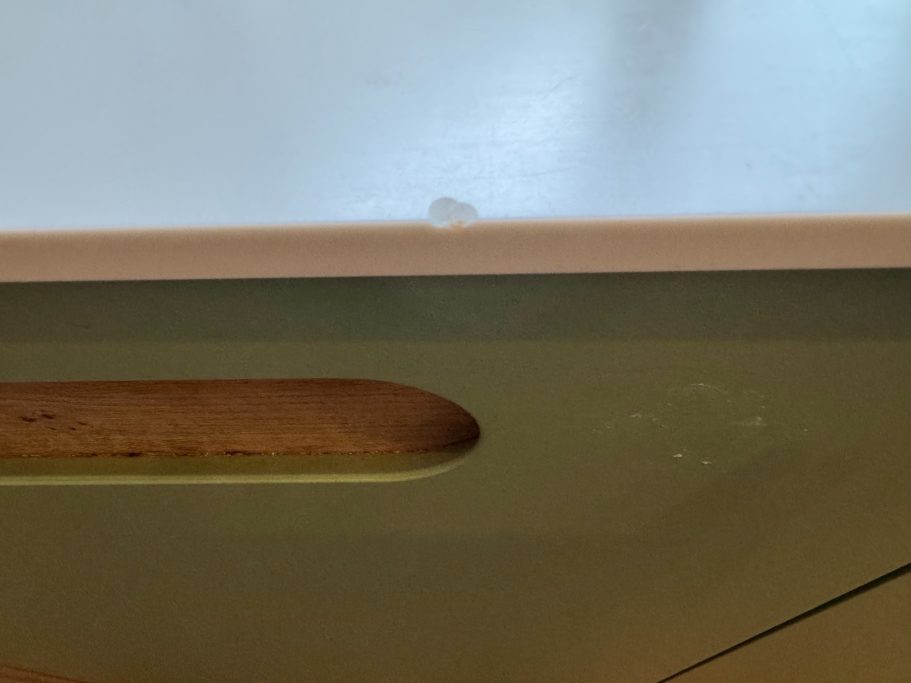 Before repair: missing section of Corian A speckled beige Corian worktop with a large chunk missing from the surface due to a large object being dropped on it.