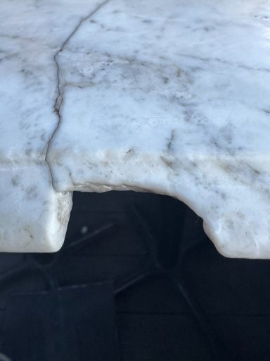 This picture shows a large piece missing from the edge of a marble vanity top. This needs refilling, sanding, and reshaping. White marble vanity top edge is completely smashed due to a heavy bottle of perfume that was dropped on the edge, cracking the worktop.