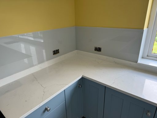 Marble effect worktops with a glass splashback sat ontop of the upstand with 2 cut outs for sockets.