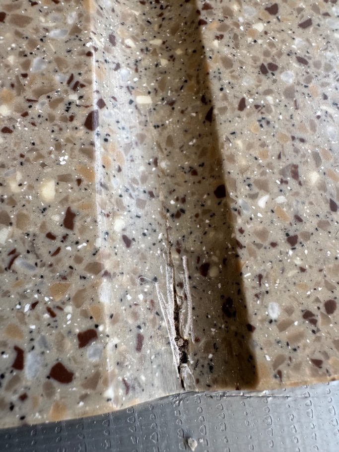 The worktop has a crack in the draining groove area, extending deep into the material. Crack in the Corian worktop located at the draining groove area in Harrogate, Leeds.