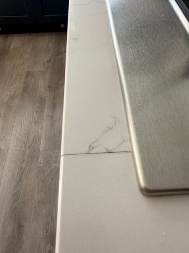 "The white marble look of a quartz worktop joint at the Hob area had come apart." "Picture showing a white quartz worktop with a joint at the hob area. This hob run has dropped, and the joint has opened up."