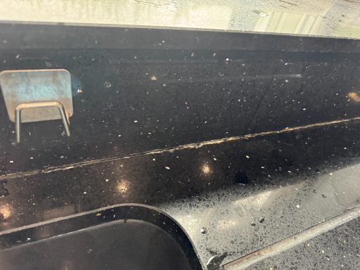 Silicone coming out of the worktop due to age. Black worktop showing signs of old silicone coming out of the sealed Joint