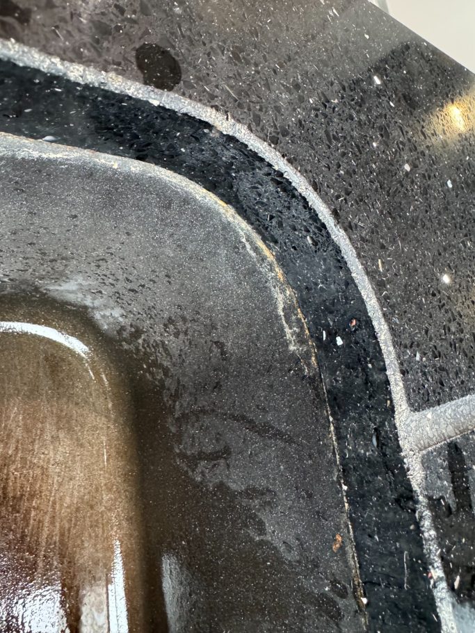 Before repair: deteriorated sink joint seal Sparkly black kitchen Worktop Sink area showing signs of silicone coming out of Joint this was because of its age.